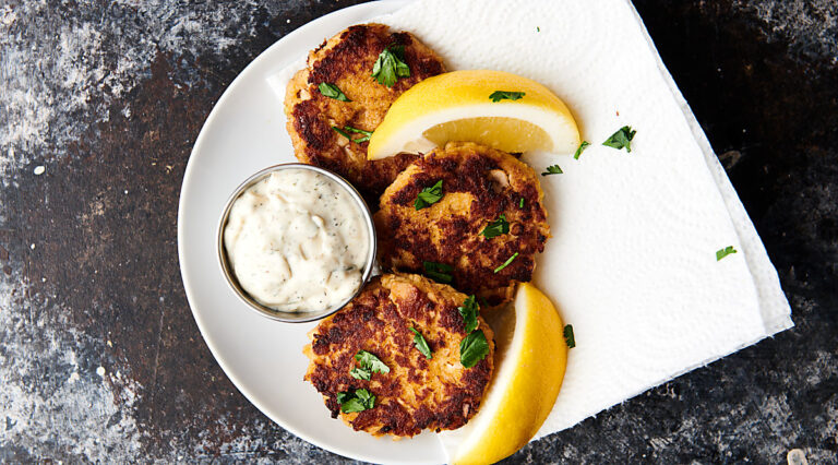 Plate of three salmon patties with tartar sauce and lemon slices from above