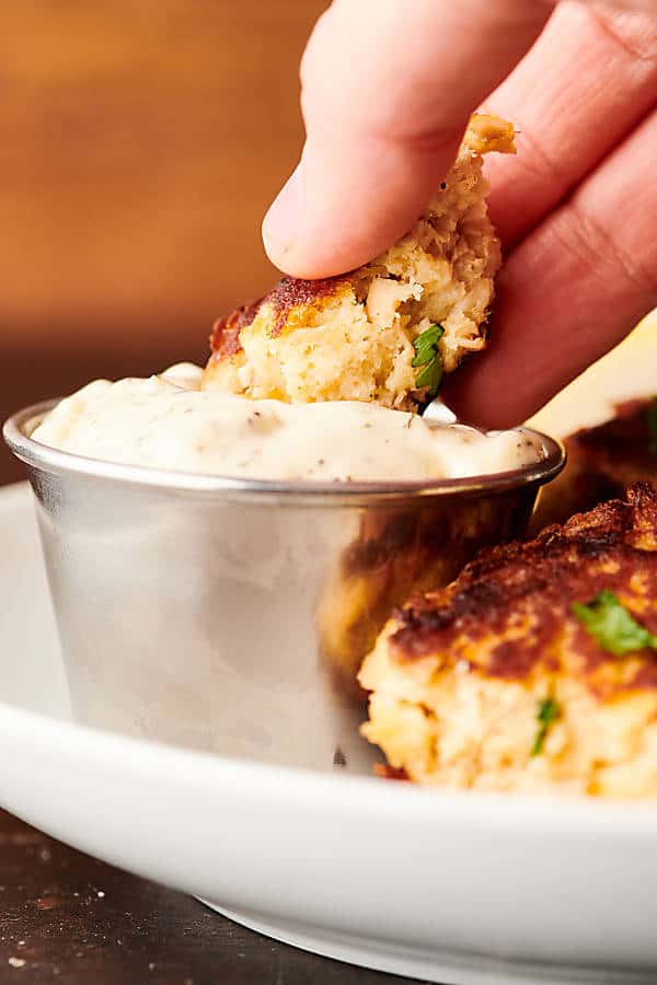 Salmon patty being dipped into cup of sauce