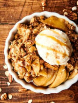 Dish of apple crisp recipe with ice cream and caramel drizzle above