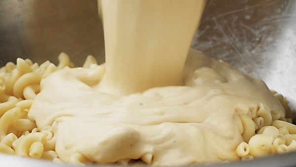 Cheese sauce being poured over macaroni noodles
