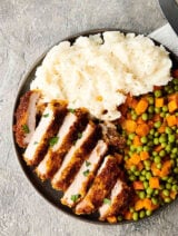 Plate of sliced pork chop, peas and carrots, and mashed potatoes above