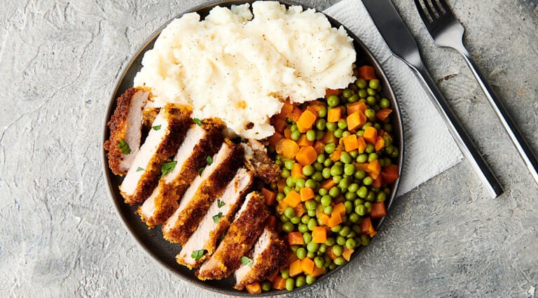 Plate of sliced pork chop, mixed peas and carrots, and mashed potatoes above