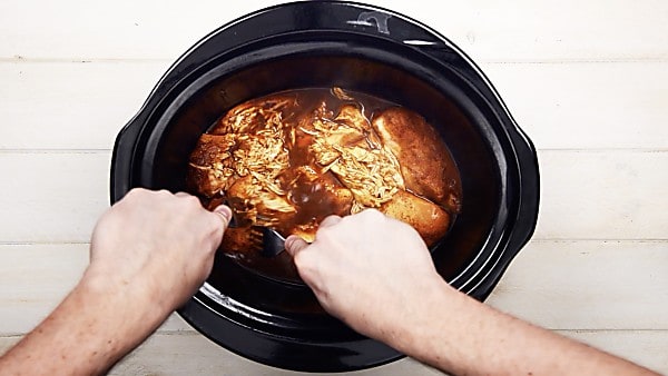 crock pot mexican chicken being shredded with two forks