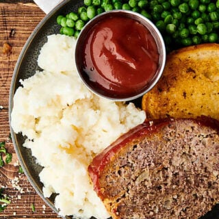 Plate of meatloaf, mashed potatoes, ketchup, peas, and texas toast above