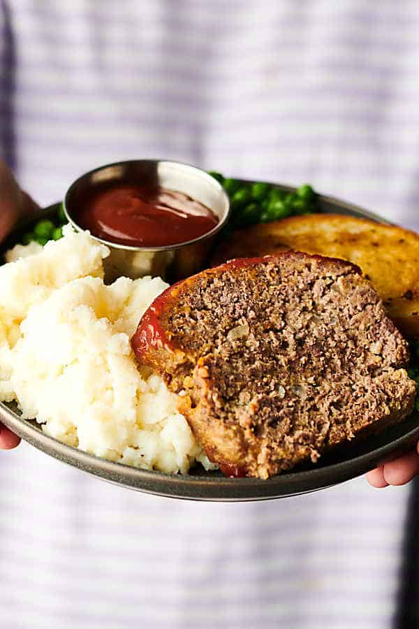 Plate of meatloaf, mashed potatoes, ketchup, texas toast, and ketchup held