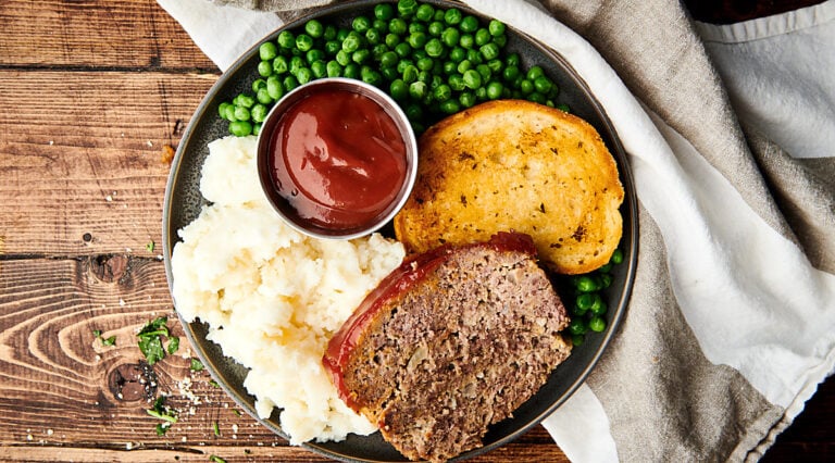 Plate of meatloaf, mashed potatoes, texas toast, peas, and ketchup above