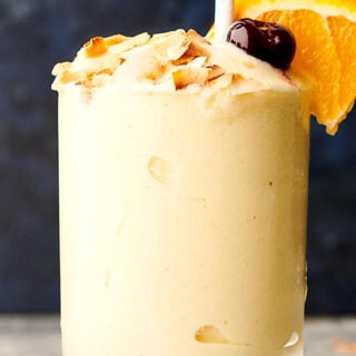 Cup of tropical smoothie with toasted coconut, cherry, straw, and orange slice
