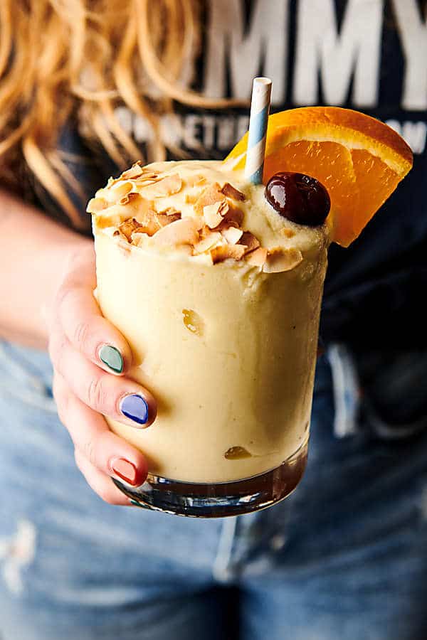 Tropical smoothie with toasted coconut, cherry, straw, and orange slice held