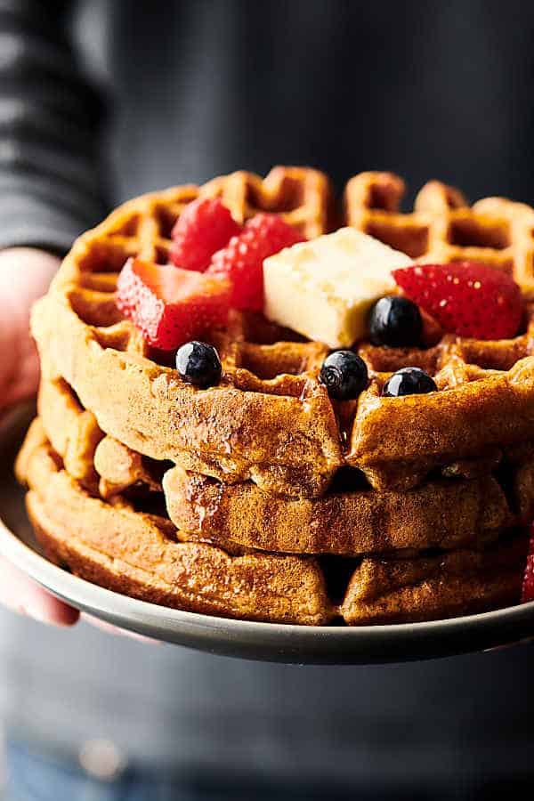 Plate of 3 stacked waffles with butter, strawberries, and blueberries held