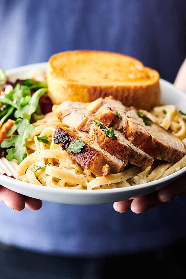 plate of chicken alfredo with side salad and garlic bread held two hands