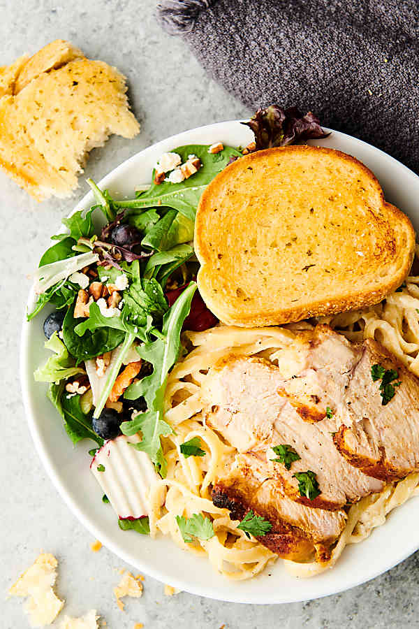 plate of chicken alfredo with side salad and garlic bread above