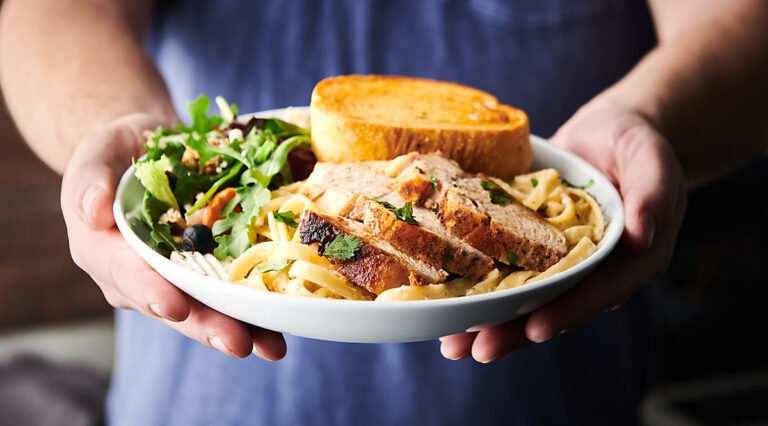 plate of chicken alredo held two hands