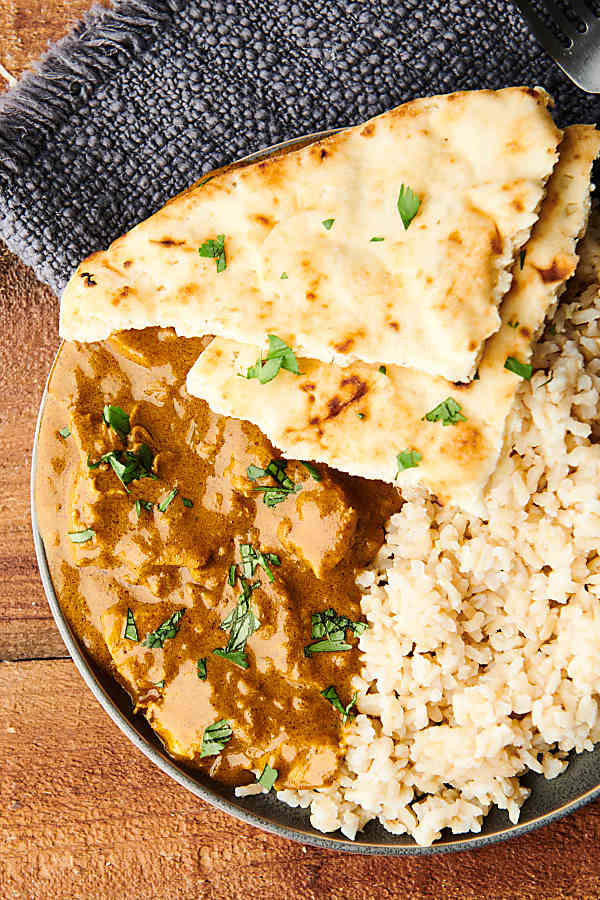 Chicken curry on a plate with naan and rice above