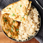 Chicken curry on a plate with rice and naan above