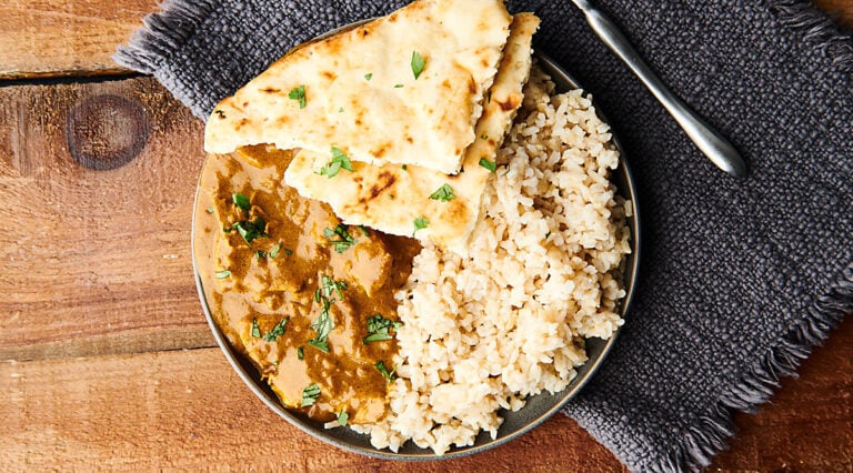 Chicken curry on a plate with rice and naan above