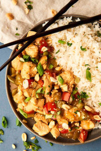 plate of kung pao chicken and rice with chopsticks above