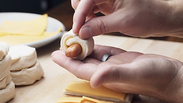 mini hot dog being rolled into dough with cheese