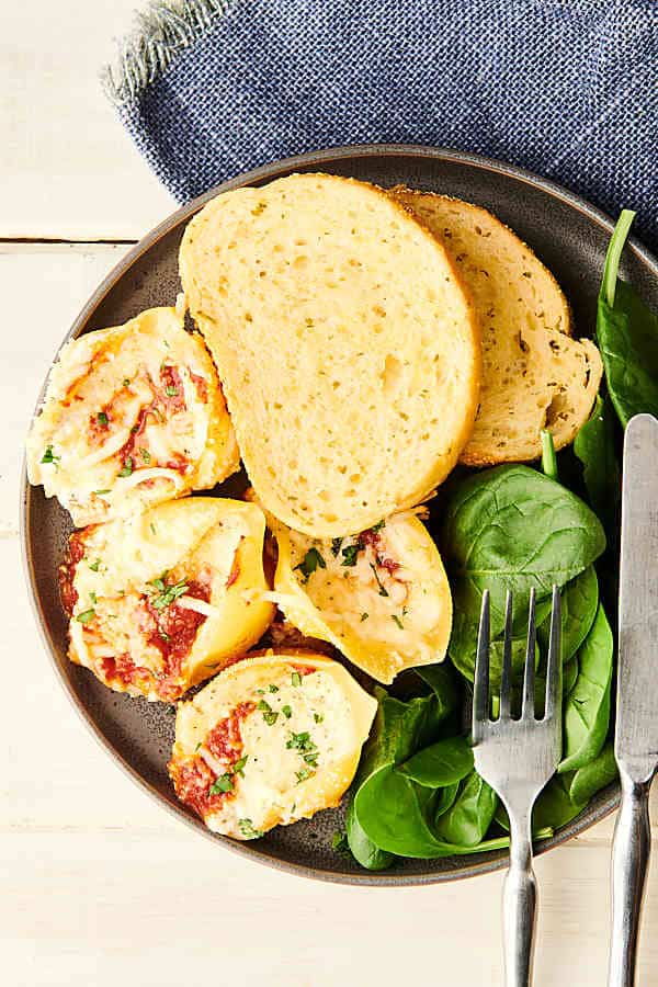 Stuffed shells on a plate with garlic bread and spinach above