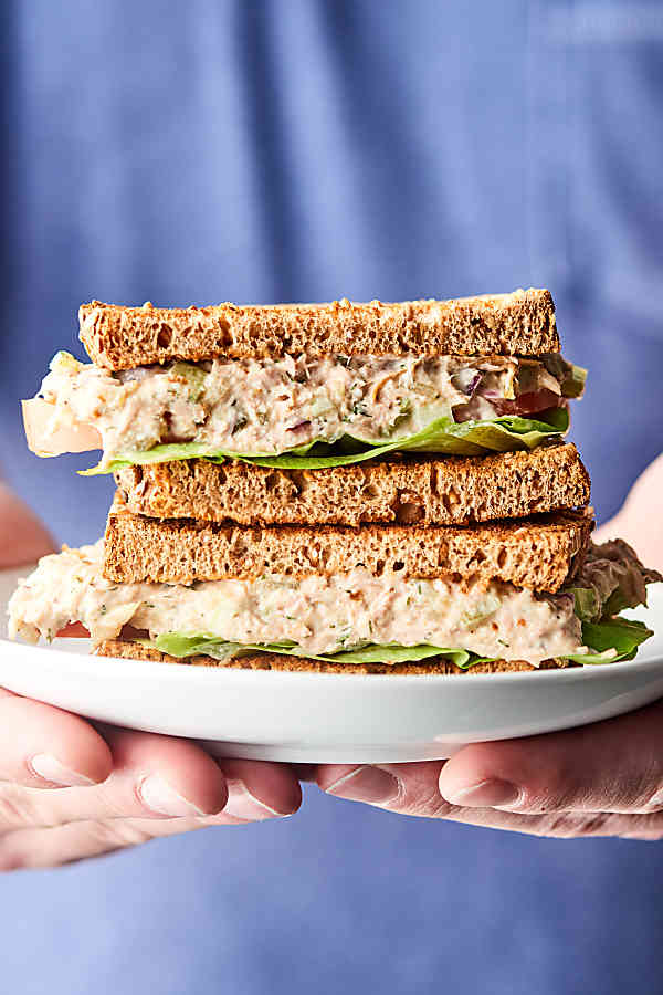 Two halves tuna salad sandwich stacked on a plate held