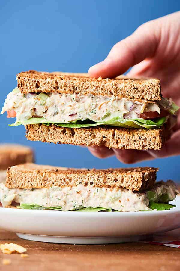 Tuna salad sandwich one half held, other on plate