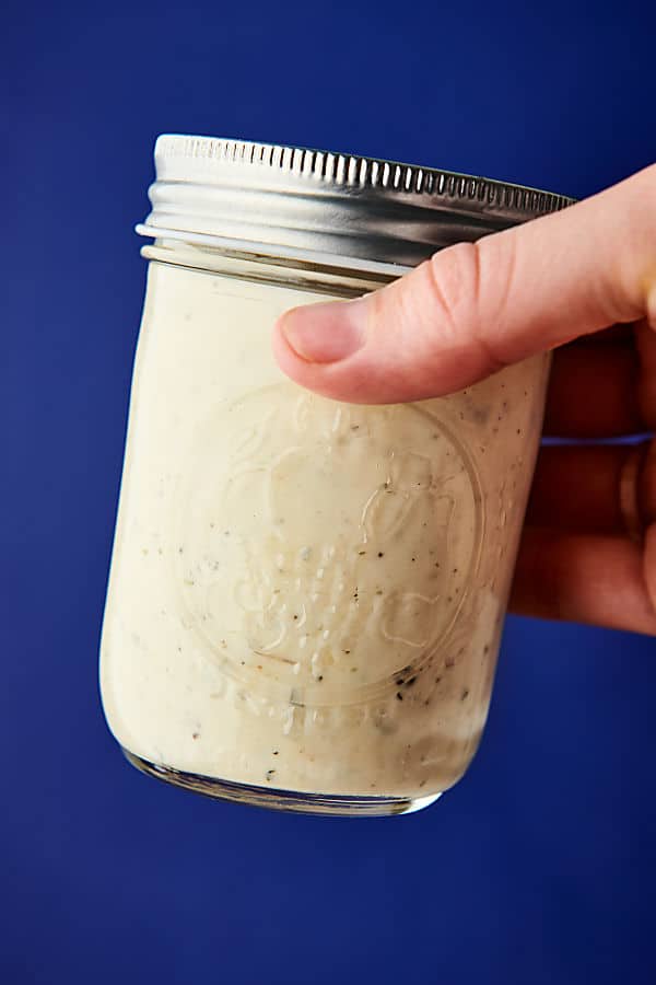 jar of alfredo sauce held blue background
