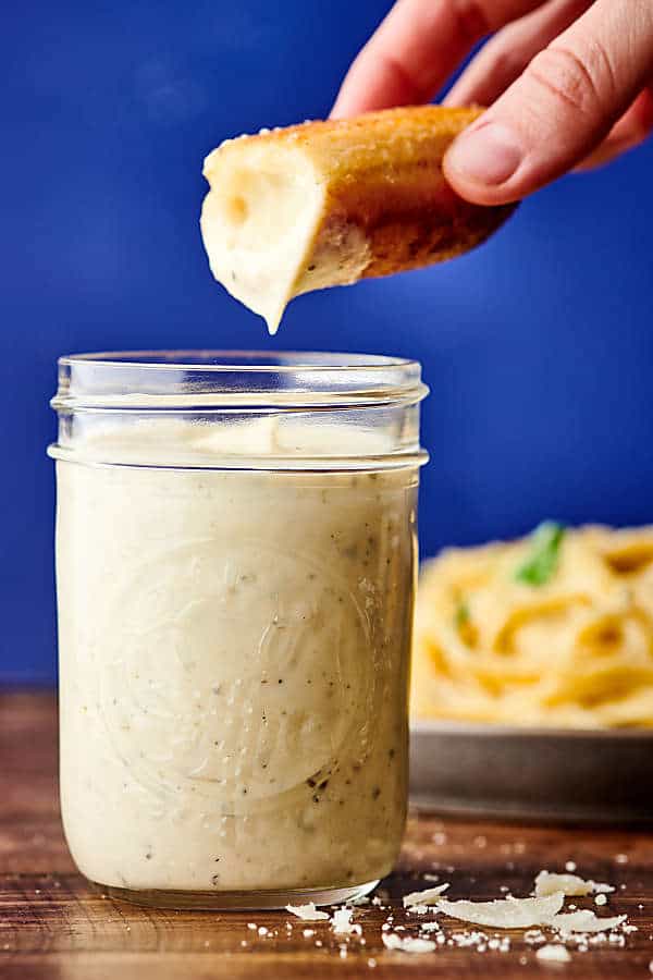 breadstick being dipped in jar of alfredo sauce