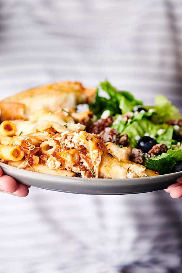 plate of baked ziti with side salad held two hands