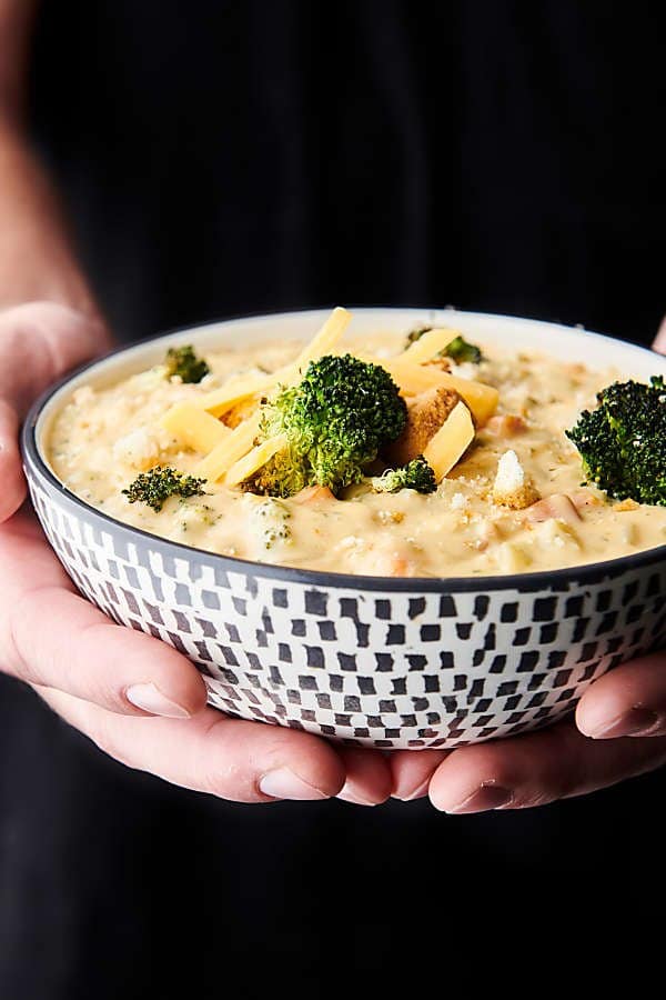 bowl of broccoli cheddar soup held two hands