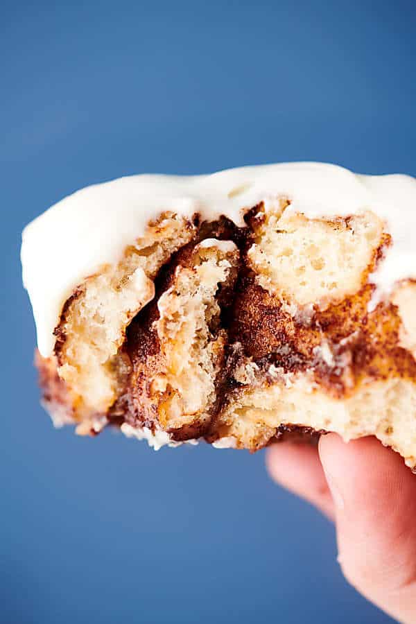 cinnamon roll with bite out held blue background