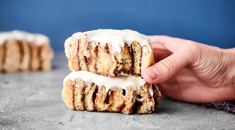 two cinnamon rolls stacked, one being picked up