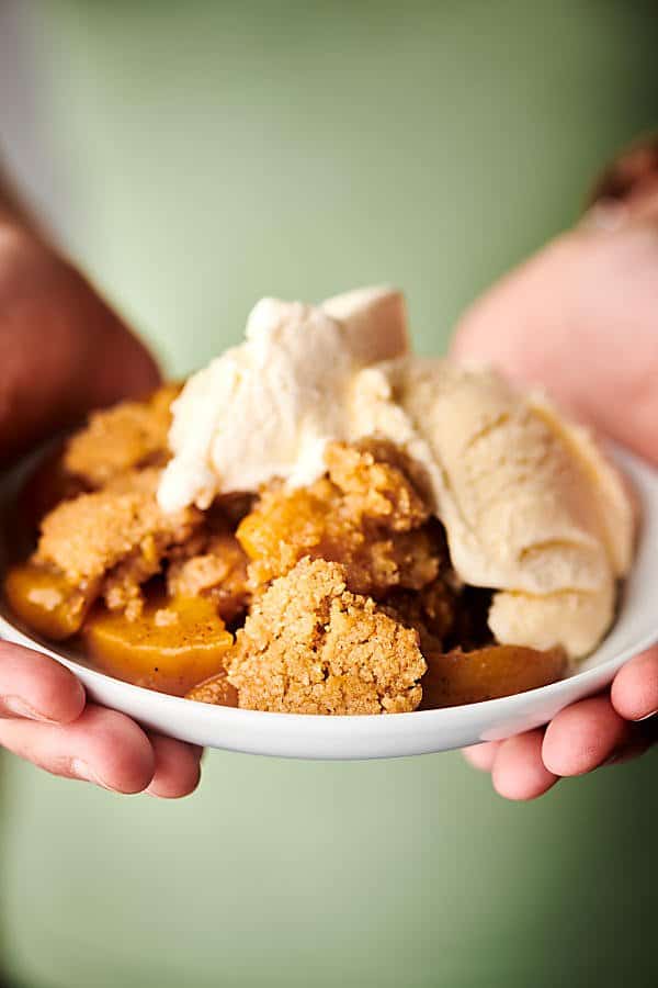 plate of peach cobbler held two hands