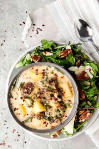 bowl of zuppa toscana on plate with salad above