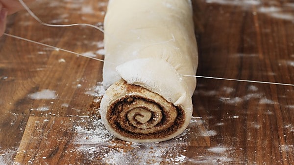 cinnamon roll dough being cut with floss