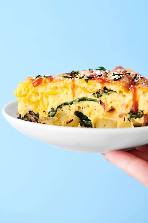 slice of frittata on plate held, blue background