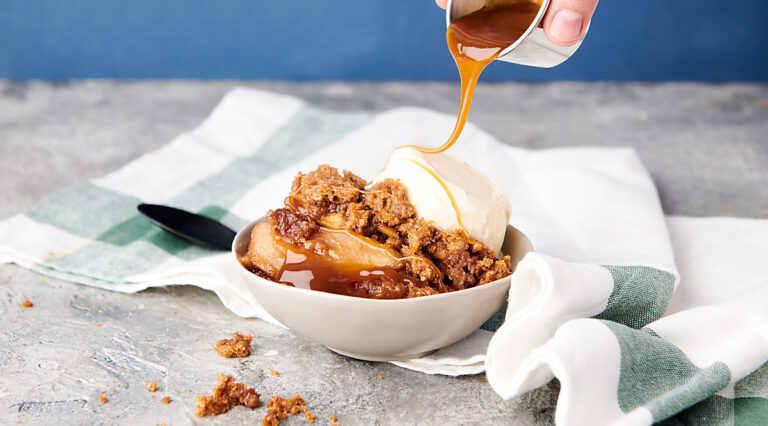 caramel being drizzled over bowl of apple crumble with ice cream