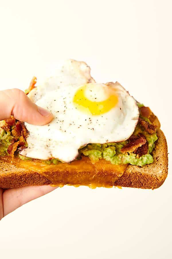 bacon, egg, and cheese avocado toast held