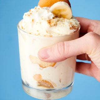 cup with banana pudding held blue background