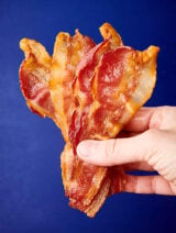 slices of bacon held blue background