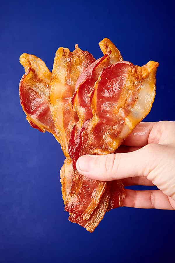 slices of bacon held blue background