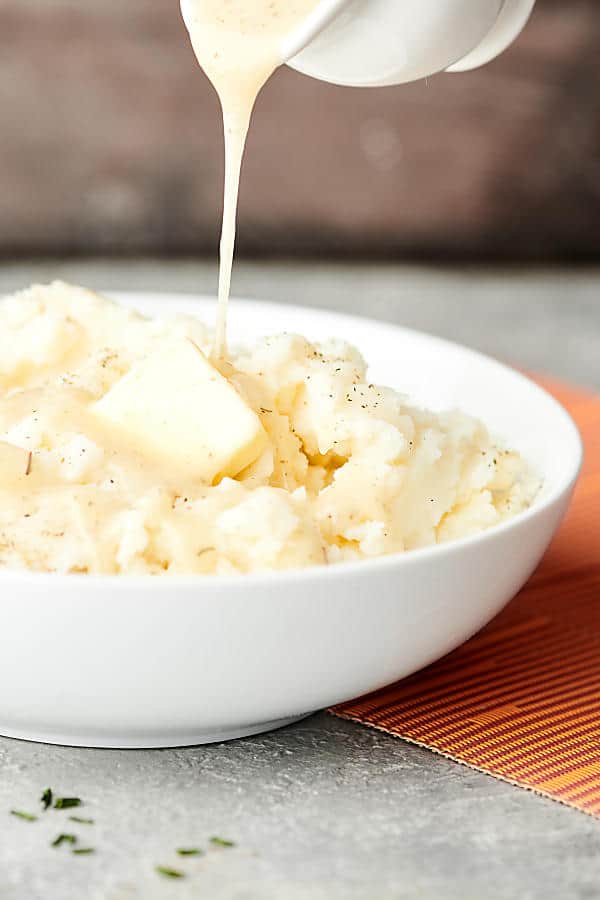 gravy being drizzled over bowl of mashed potatoes