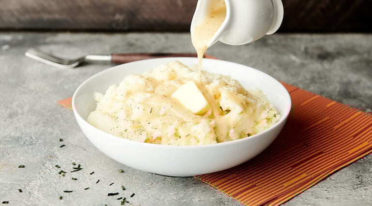 gravy being drizzled over bowl of mashed potatoes