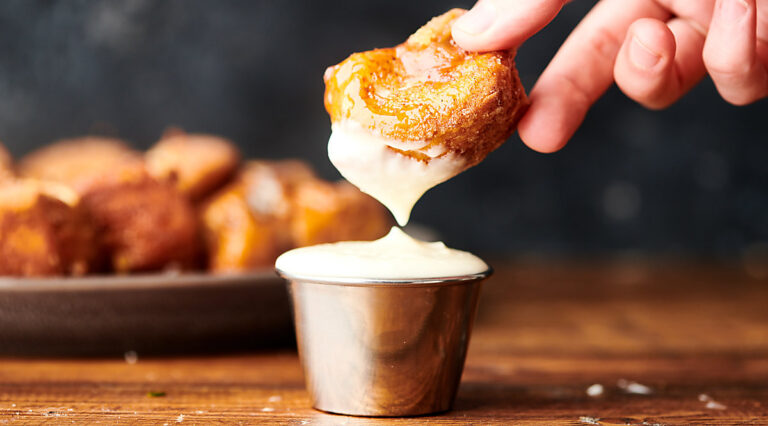 piece of monkey bread being dipped into frosting