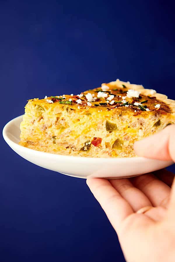 slice of quiche on plate held blue background