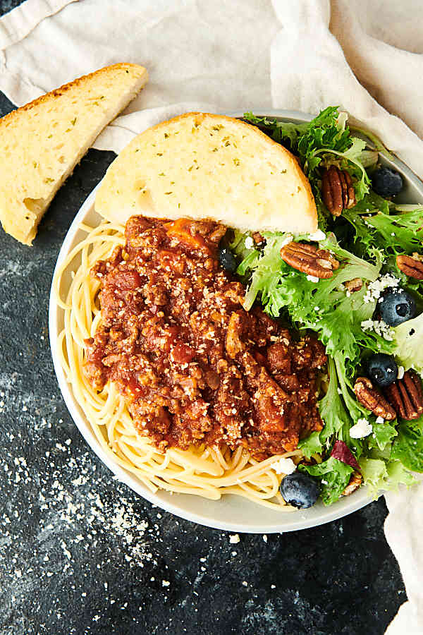 plate of spaghetti bolognese with garlic bread and salad above
