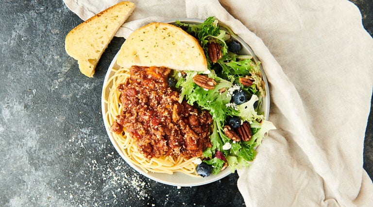 spaghetti bolognese on plate with salad and garlic bread above