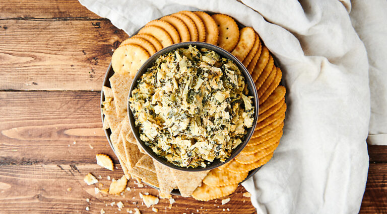 spinach artichoke dip in bowl on plate with crackers above