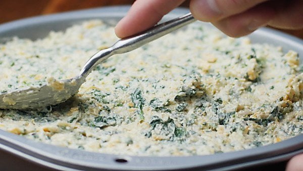 spinach artichoke dip being spread into baking dish