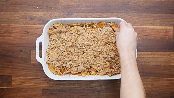 apple mixture in baking dish, crumble being sprinkled on top