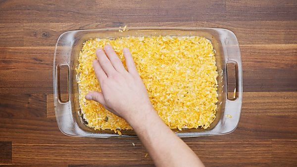 chicken and cheese mixture in baking dish being topped with shredded cheese