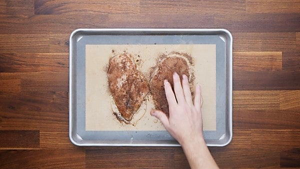 chicken breast on baking sheet with seasonings